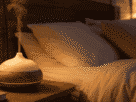 Quarto aconchegante à noite com difusor de aromaterapia liberando vapor suave, representando o uso de óleos essenciais para dormir, com iluminação quente e roupa de cama em tons neutros.