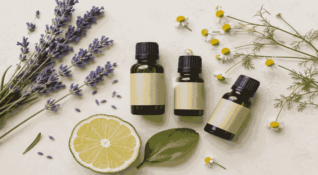 Três frascos de óleos essenciais para dormir em composição flat lay, acompanhados de flores de lavanda, camomila e fatia de bergamota sobre fundo claro e minimalista.