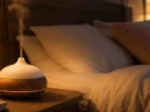 Quarto aconchegante à noite com difusor de aromaterapia liberando vapor suave, representando o uso de óleos essenciais para dormir, com iluminação quente e roupa de cama em tons neutros.